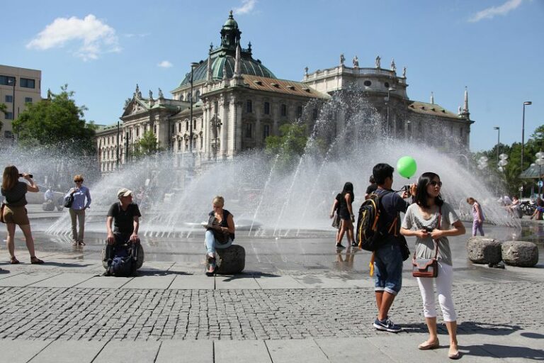 Schulklasse Klassenfahrt München Führung Justizpalast Auf dem Bild sehen wir den Blick über den Stachusspringbrunnen auf den Münchner Justizpalast. Im Vordergrund Personen.