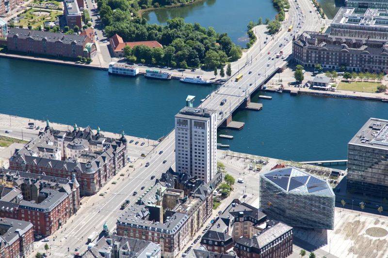 Während der Klassenfahrt nach Kopenhagen übernachtet die Schulklasse im Danhostel Copenhagen City. Auf dem Bild sehen wir das Hochhaus des Hostels aus der Luft aufgenommen. Im Hintergrund Brücken, Kanäle und die City.